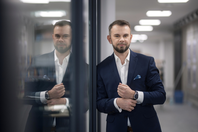 Energetyka wiatrowa | Studia podyplomowe w Bydgoszczy | Uniwersytet WSB Merito Bydgoszcz: Główna grafika: Toruń - studia podyplomowe - Uczestnik studiów podyplomowych pozujący do zdjęcia z odbiciem w oknie