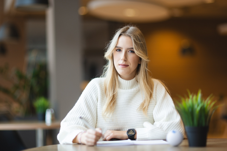 Erasmus+ Mobilność pracowników administracyjnych i dydaktycznych w celu udziału w szkoleniu | Uniwersytet WSB Merito Bydgoszcz: Studentka WSB Merito Bydgoszcz siedzi przy stole robiąc notatki w przytulnym pomieszczniu