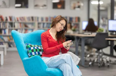Search results | WSB Merito Gdańsk University: Studentka w bibliotece siedzi na wygodnym fotelu i korzysta z komórki