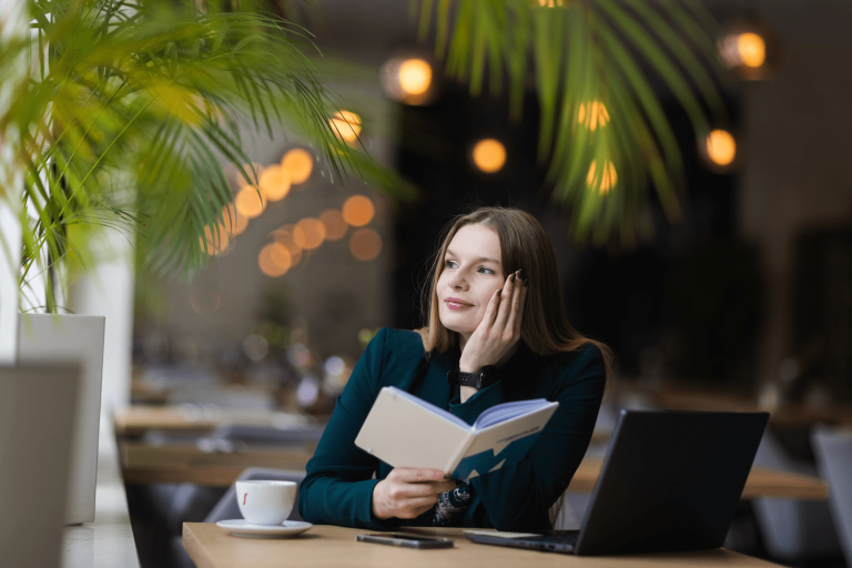 Search results | WSB Merito Gdańsk University: Portret młodej, naturalnej kobiety o delikatnych rysach i włosach. Siedzi przy biurku w kawiarni oparta dłonią o głowę, w drugiej ręce trzyma zeszyt z logotypem UWSB Merito