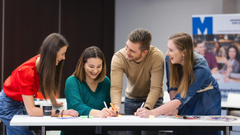 grupa uśmiechniętych studentów pracująca nad projektem przy stole