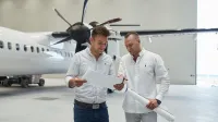 Zarządzanie portami lotniczymi (z certyfikatem Portu Lotniczego im. Lecha Wałęsy) | Studia I stopnia w Gdańsku | Uniwersytet WSB Merito w Gdańsku: Dwóch ubranych na jasno mężczyzn patrzy na kartkę i znajdują się w przestrzeni, gdzie jest samolot