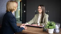 Zarządzanie w administracji publicznej | Studia II stopnia ze studiami podyplomowymi  | Uniwersytet WSB Merito w Gdańsku: Dwie kobiety siedzą przy biurku naprzeciwko siebie i załatwiają sprawy administracyjne