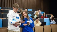 Programowanie desktop apps | Studia II stopnia w Gdańsku | Uniwersytet WSB Merito w Gdańsku: Studenci w auli, chłopak i dziewczyna pokazują sobie coś na komórce