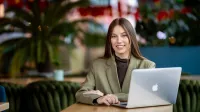 Management | Studia I stopnia w Gdańsku | Uniwersytet WSB Merito w Gdańsku: Studentka ubrana w oliwkową marynarkę siedzi w kawiarni przy laptopie