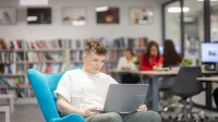 Prompting i optymalizacja systemów AI | Studia I stopnia w Gdańsku | Uniwersytet WSB Merito w Gdańsku: Student siedzi na fotelu z laptopem na kolanach w bibliotece