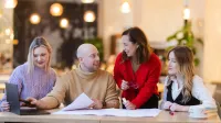 Nowoczesne przywództwo, zarządzanie oparte na danych i skuteczne projekty – liderzy Publicznych Służb Zatrudniania w działaniu | Studia podyplomowe w Gdańsku | Uniwersytet WSB Merito w Gdańsku: Studenci pracują w grupie w przestrzeni o ciepłym pomarańczowym świetle
