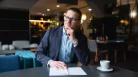 Projektowanie interfejsów graficznych | Studia podyplomowe w Gdańsku | Uniwersytet WSB Merito w Gdańsku: Mężczyzna w ubraniu biznesowym siedzi przy biurku z filiżanką kawy