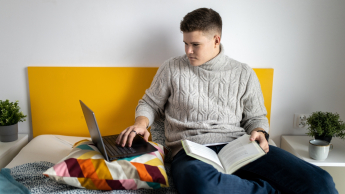 Software Development | Studia I stopnia w Gdańsku | Uniwersytet WSB Merito w Gdańsku: Student siedzi w łóżku z laptopem i ma na kolanach książkę
