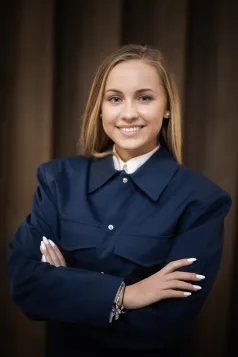 Szkoły | Uniwersytet WSB Merito w Gdańsku: Zdjęcie młodej dziewczyny o blond włosach i dużym białym uśmiechu. Ma ona na sobie granatową marynarkę