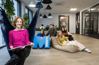 ABC Studenta | Uniwersytet WSB Merito w Gdańsku: Studentka na hamaku siedzi z książką, za nią grupa studentów z sygnetem M