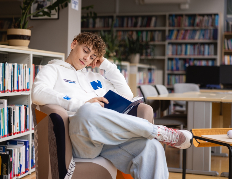 Drony i technologie bezzałogowe w obszarze bezpieczeństwa | Studia I stopnia w Gdańsku | Uniwersytet WSB Merito w Gdańsku: Student na fotelu czyta książkę w bibliotece