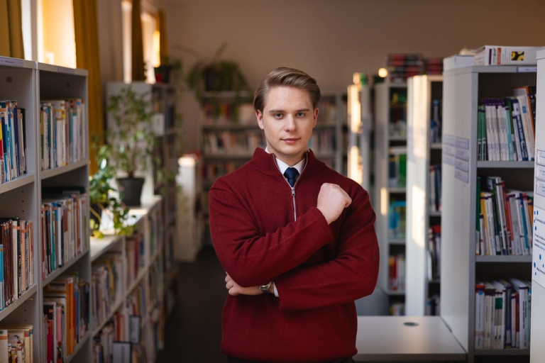 Rachunkowość i finanse przedsiębiorstw | Studia I stopnia w Gdańsku | Uniwersytet WSB Merito w Gdańsku: Student w bibliotece. Ma na sobie sweter, a pod spodem koszulę i krawat