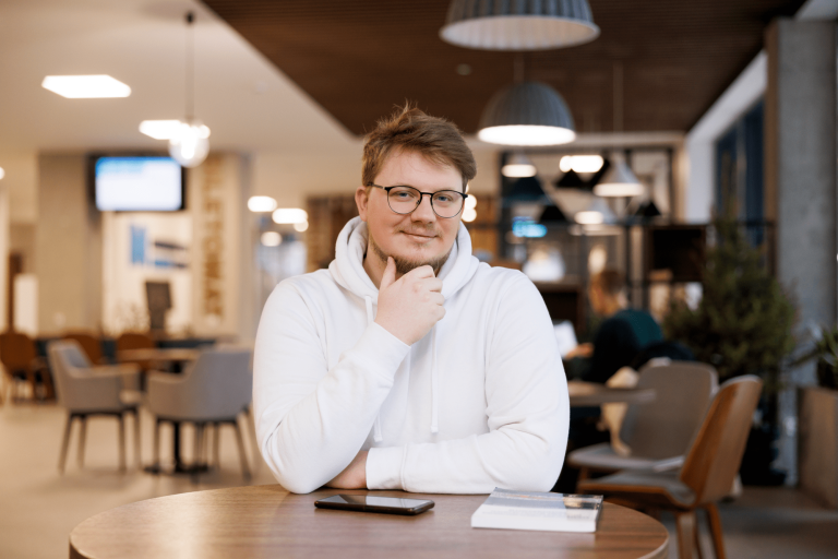 Transformacja Cyfrowa w Administracji i Biznesie | Studia II stopnia w Gdańsku | Uniwersytet WSB Merito w Gdańsku: Student w białej bluzie w holu przy stoliku 