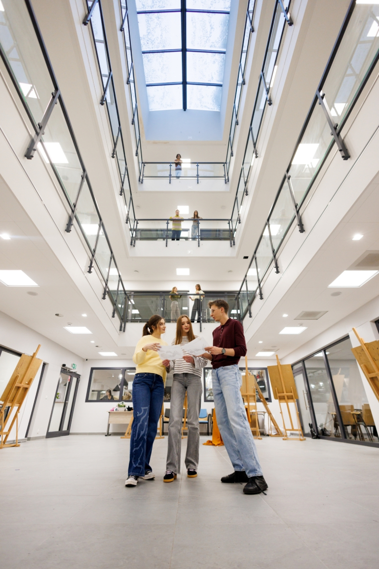 Nowoczesne pracownie i laboratoria | Uniwersytet WSB Merito w Gdańsku: Studenci stoją pośrodku atrium. Zdjęcie z perspektywy żabiej z widokiem na architekturę budynku