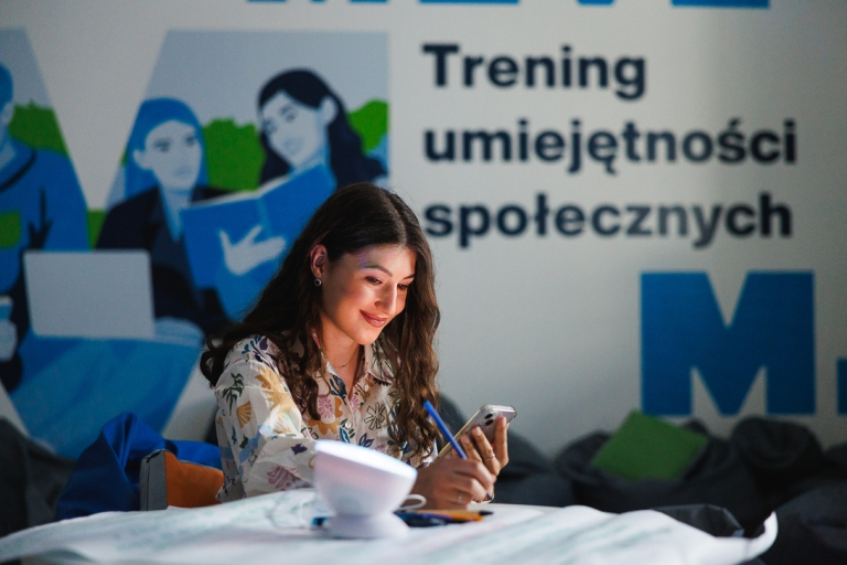 Wellbeing i bezpieczeństwo w pracy | Studia I stopnia w Gdańsku | Uniwersytet WSB Merito w Gdańsku: Studentka przy banerze treningu umiejętności społecznych