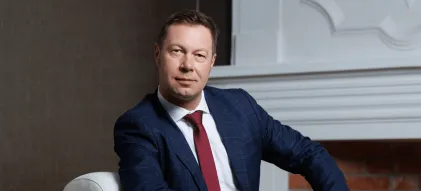 Władze uniwersytetu | Uniwersytet WSB Merito w Gdańsku: Mężyczna w pozie siedzącej, opiera rękę na kolanie, ma na sobie garnitur i bordowy krawat