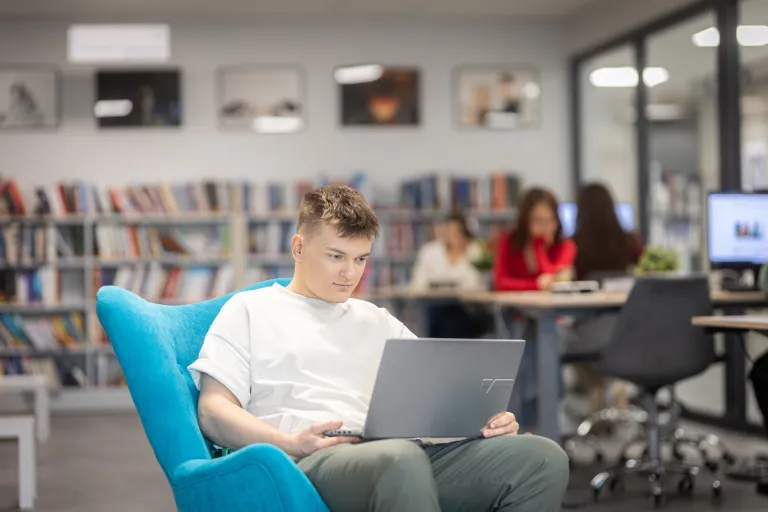 Zarządzanie portami lotniczymi (z certyfikatem Portu Lotniczego im. Lecha Wałęsy) | Studia I stopnia w Gdańsku | Uniwersytet WSB Merito w Gdańsku: Student siedzi na fotelu z laptopem na kolanach w bibliotece
