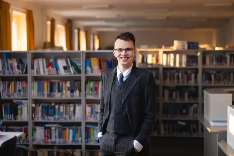 Finanse i rachunkowość | Studia II stopnia w Gdańsku | Uniwersytet WSB Merito w Gdańsku: Student w bibliotece ubrany w garnitur 