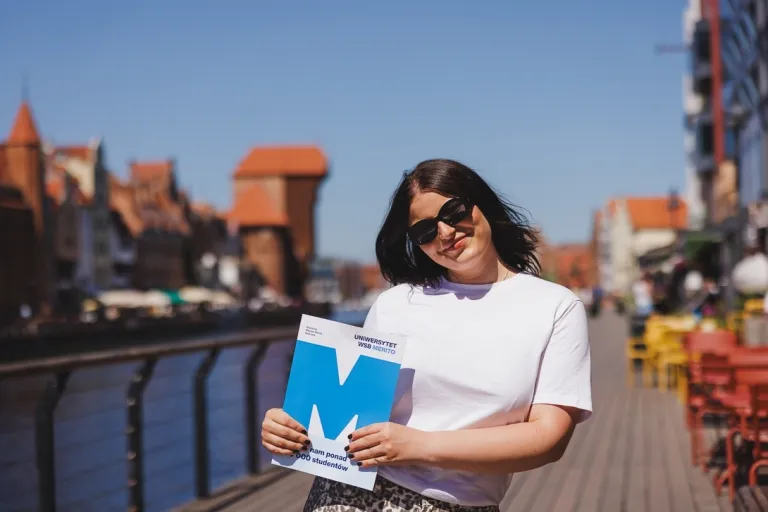Administracja publiczna | Studia I stopnia w Gdańsku | Uniwersytet WSB Merito w Gdańsku: Studentka z teczką z sygnetem M, z tyłu widać Gdańskiego Żurawia