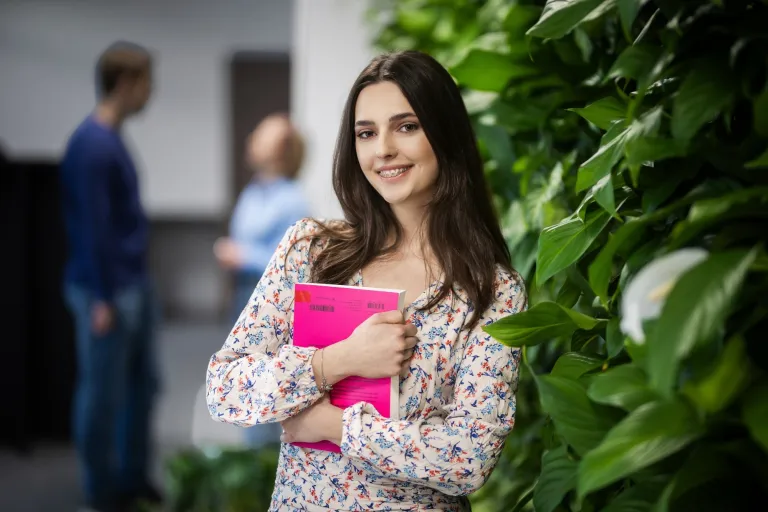 Pedagogika opiekuńczo-wychowawcza z proﬁlaktyką społeczną | Studia II stopnia w Gdańsku | Uniwersytet WSB Merito w Gdańsku: Studentka przy zielonej ścianie z książką w ręku