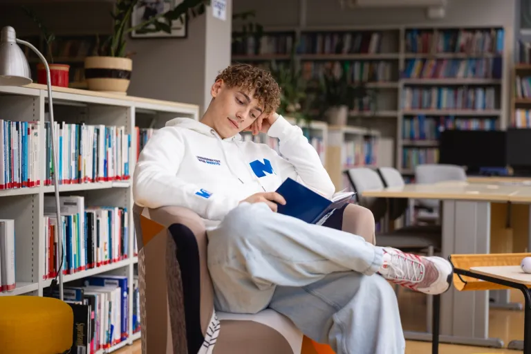 Inteligentne zarządzanie magazynem | Studia I stopnia w Gdańsku | Uniwersytet WSB Merito w Gdańsku: Student na fotelu czyta książkę w bibliotece