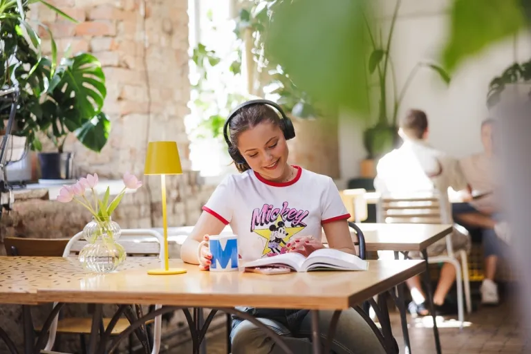 Marketing i komunikacja społeczna | Studia II stopnia ze studiami podyplomowymi  | Uniwersytet WSB Merito w Gdańsku: Studentka w słuchawkach siedzi w kawiarni przy książce