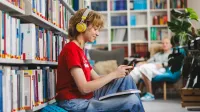 Psychologia kliniczna dzieci i młodzieży | Studia jednolite magisterskie w Gdyni | Uniwersytet WSB Merito Gdynia: Studentka ze słuchawkami w uszach, książką na kolanach i telefonem w ręku