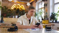 Windykacja i zarządzanie wierzytelnościami | Studia podyplomowe w Gdyni | Uniwersytet WSB Merito Gdynia: Student w kawiarni przy komórce