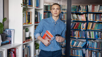 Administracja celno-skarbowa | Studia I stopnia w Gdyni | Uniwersytet WSB Merito Gdynia: Student z książkami i kawą w ręku w przestrzeni biblioteki