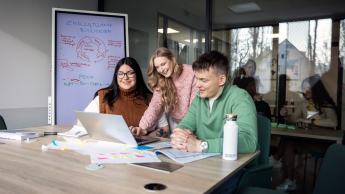 Zarządzanie | Studia I stopnia w Gdyni | Uniwersytet WSB Merito Gdynia: Trójka studentów wspólnie uczy się w bibliotece. Używają laptopa. Za nimi znajduje się tablica z ich notatkami o zarządzaniu ryzykiem.