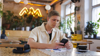 Windykacja i zarządzanie wierzytelnościami | Studia podyplomowe w Gdyni | Uniwersytet WSB Merito Gdynia: Student w kawiarni przy komórce