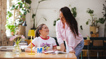 Zarządzanie projektami | Studia I stopnia w Gdyni | Uniwersytet WSB Merito Gdynia: Dziewczyna pochyla się nad stołem przy, którym siedzi studentka