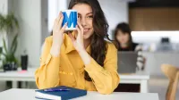 Business English | Studia podyplomowe w Łodzi | Uniwersytet WSB Merito Łódź: Uśmiechnięta dziewczyna trzyma kubek "Merito" przy twarzy.