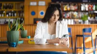 E-marketing | Studia I stopnia w Łodzi | Uniwersytet WSB Merito Łódź: Studentka przegląda telefon przy filiżance kawy.