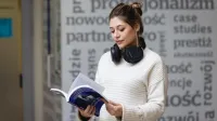 Psychologia reklamy i komunikacji | Uniwersytet WSB Merito Łódź: Kobieta w białym swetrze czyta książkę w nowoczesnym wnętrzu uczelni, z hasłami o profesjonalizmie w tle.
