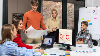 Marketing i sprzedaż | Studia I stopnia w Łodzi | Uniwersytet WSB Merito Łódź: Grupa młodych osób analizuje dane i wykresy podczas zespołowej pracy nad projektem logistycznym w nowoczesnym biurze.