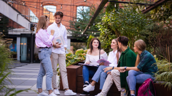 Zielone technologie i sztuczna inteligencja: informatyka dla zrównoważonego rozwoju | Studia podyplomowe w Łodzi | Uniwersytet WSB Merito Łódź: Sześcioro studentów WSB Merito rozmawia przy budynku z czerwonej cegły wśród zieleni