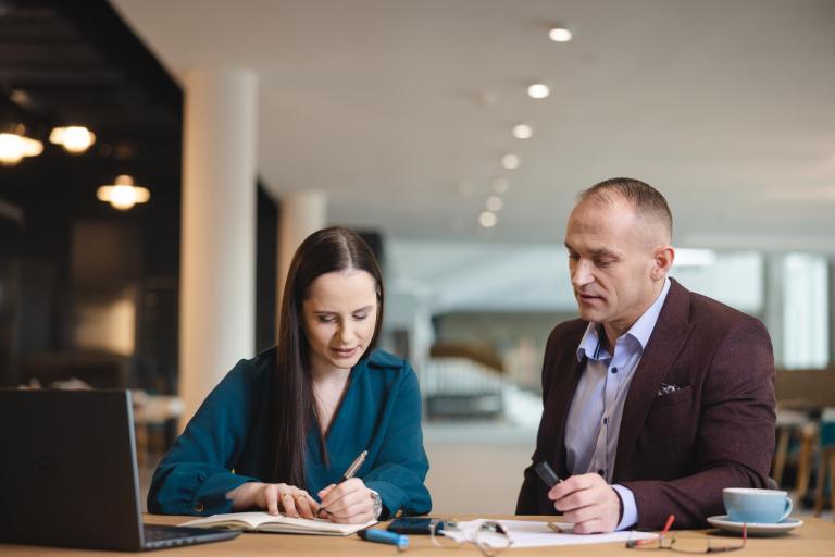 Gospodarowanie nieruchomościami | Studia I stopnia w Łodzi | Uniwersytet WSB Merito Łódź: Kobieta i mężczyzna siedzą przy stole w nowoczesnym wnętrzu, wspólnie analizując notatki i dokumenty.