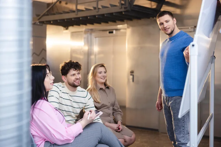 Zarządzanie zasobami ludzkimi | Studia II stopnia w Łodzi | Uniwersytet WSB Merito Łódź: Student prezentuje na tablicy, a trójka słucha.