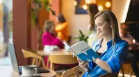 Media i komunikacja w biznesie | Studia I stopnia w Opolu | Uniwersytet WSB Merito Opole: Dziewczyna siedzi w kawiarni i czyta notatki. na stoliku stoi laptop i kawa