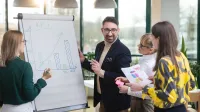 Planowanie produkcji – nowoczesne   narzędzia: SAP S/4HANA, Siemens Opcenter APS | Uniwersytet WSB Merito Opole: Główna grafika: Opole - studia podyplomowe - Planowanie produkcji – nowoczesne   narzędzia: SAP S/4HANA, Siemens Opcenter APS - Grupa osób rozpisująca wykresy przy białej tablicy