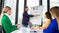 Zarządzanie jakością w branży automotive | Studia podyplomowe w Opolu | Uniwersytet WSB Merito Opole: Główna grafika: Opole - studia podyplomowe - Zarządzanie jakością w branży automotive - grupa osób słuchająca wypowiedzi mężczyzny stojącego przy tablicy