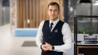 Pentester - specjalista ds. cyberbezpieczeństwa | Studia podyplomowe w Opolu | Uniwersytet WSB Merito Opole: Pentester - specjalista ds. cyberbezpieczeństwa - mężczyzna  w kawiarni, stoi obok regału na książki