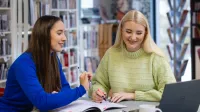 Główna grafika: Opole - studia podyplomowe - Audyt wewnętrzny i controlling - Dwie kobiety wspólnie robiące notatki