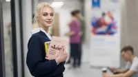 Kosmetologia anti-aging | Studia I stopnia w Opolu | Uniwersytet WSB Merito Opole: Główna grafika: Opole - studia I stopnia - specjalność Kosmetologia anti-aging - Dziewczyna stojąca na korytarzu, trzyma pod ręką książki