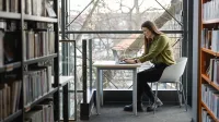 Główna grafika: Opole - studia podyplomowe - Trener języków obcych - Kobieta siedząca w bibliotece