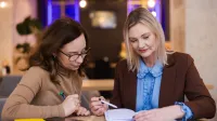 Główna grafika: Opole - studia podyplomowe - Terapia uzależnień - uczestniczki studiów podyplomowych analizują wspólnie notatki z zeszytu