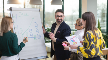 Planowanie produkcji – nowoczesne   narzędzia: SAP S/4HANA, Siemens Opcenter APS | Studia podyplomowe w Opolu | Uniwersytet WSB Merito Opole: Główna grafika: Opole - studia podyplomowe - Planowanie produkcji – nowoczesne   narzędzia: SAP S/4HANA, Siemens Opcenter APS - Grupa osób rozpisująca wykresy przy białej tablicy