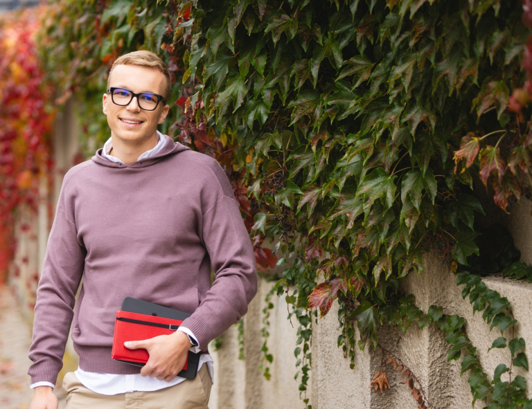 Pedagogika szkolna z doradztwem zawodowym | Studia II stopnia ze studiami podyplomowymi  | Uniwersytet WSB Merito Opole: Student stojący na zewnątrz, trzyma książki